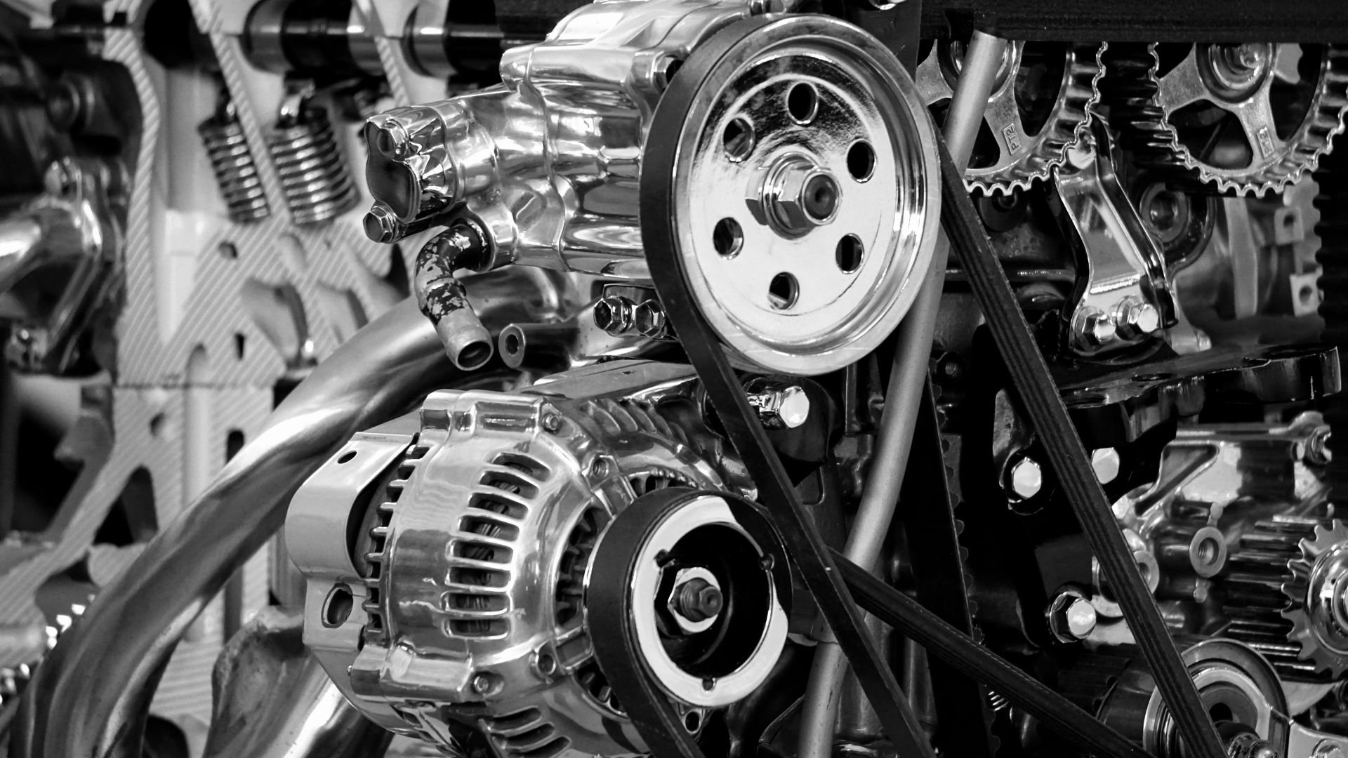 Black and white close-up of a complex automotive engine with gears and pulleys