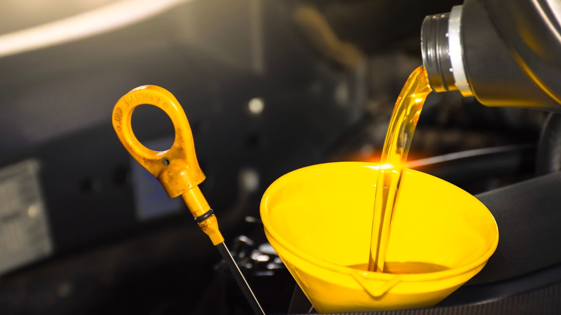 Yellow oil being poured into car engine with dipstick