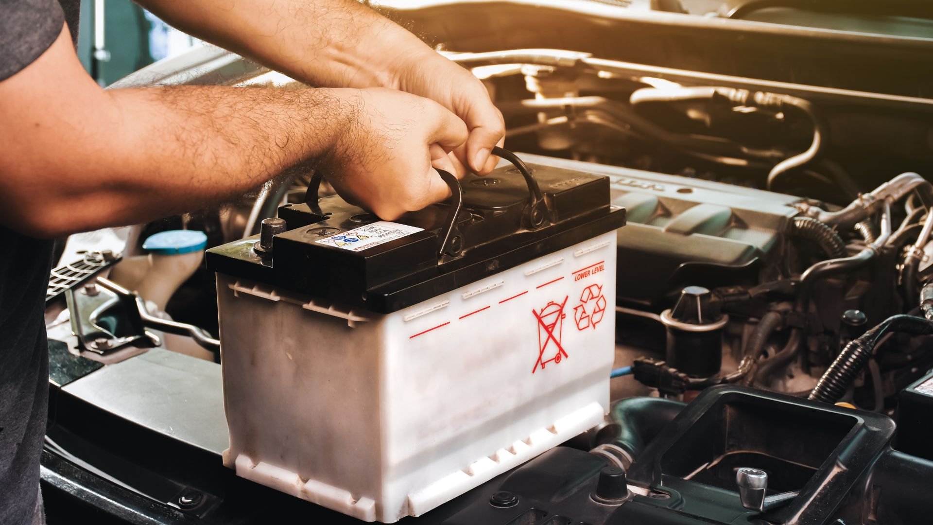Hands installing car battery in vehicle engine compartment