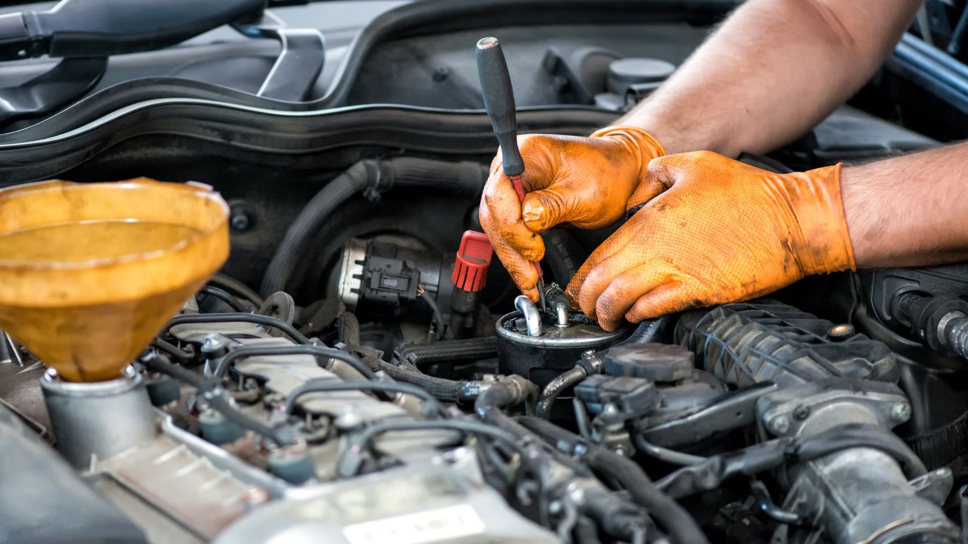 Mechanic in orange gloves repairing car engine with wrench