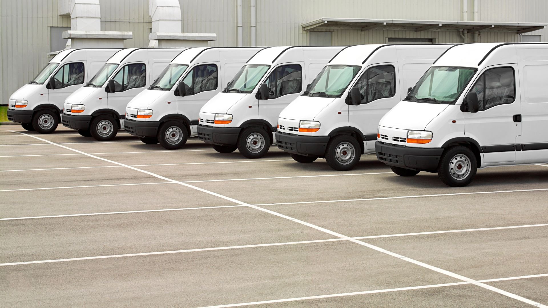 Seven white delivery vans parked in a neat row on a parking lot